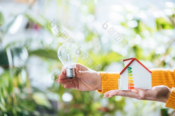 在女性手中选择性聚焦 led 灯和纸箱房模型, 在家里的能源效率概念