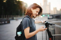 年轻快乐的女人租摩托车用手机应用在智能手机，现代交通工具在大城市