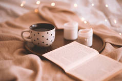 打开书本，在床头柜里的针织布上放上一杯茶和蜡烛。-早上好早餐时间。秋季季节.
