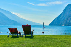 夏天, 人们坐在海滩上坐在躺椅上, 欣赏加尔达湖, 欣赏被山脉包围的美丽加尔达湖的景色