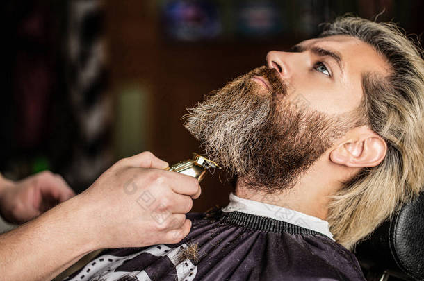 理发师带着胡子钳工作.Hipster的客户正在理发有胡子剪子的理发师的手，特写。<strong>理发店</strong>里有胡子的男人在<strong>理发店</strong>拜访理发师的男人