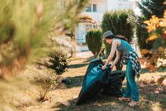 环境污染和地球日的概念。妇女自愿在公园的房子前面做清扫工作。她把垃圾袋堆在一起了。靠近点.