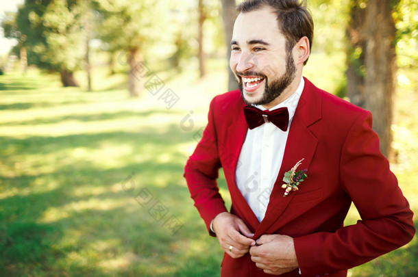 时尚新郎礼服笑西装萨拉红色、 酒红色领结。扣他的夹克在户外的人。专业的发型，胡子，小胡子。婚礼的筹备工作，准备好。复制文本的空间.