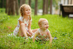 两个迷人的姐妹金发女孩拥抱和笑在草地上