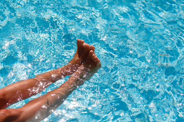 蓝色的水中的女性脚。水池里<strong>嬉戏</strong>的脚。蓝池里的水是从女性腿部的水花。妇女的腿玩在泳池里的水。游泳池中<strong>嬉戏</strong>的女人.