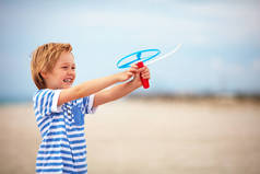 年轻快乐的男孩，孩子发射玩具螺旋桨，夏天海滩上玩乐