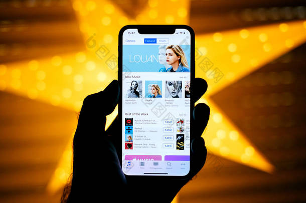 巴黎, 法国-2017年11月10日: 男子手持新的苹果 iphone X 10 显示与黄色星散背景以最佳的星期 itunes Louane 图