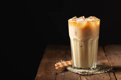 冰咖啡在一个高大的玻璃与奶油倒在和咖啡豆在一个古老的质朴的木桌上。冰冷的夏日饮料, 在黑色的木质背景上复制空间.
