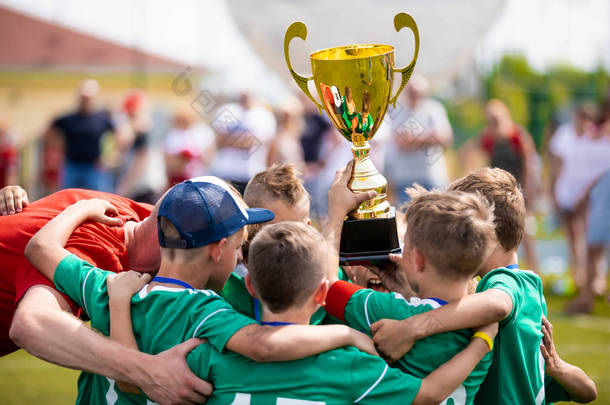 抱着奖杯的年轻足球运动员。男孩们庆祝足球足球冠军。为孩子儿童赢得团队的体育比赛.