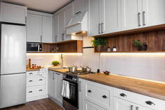 时尚的浅灰色厨房内饰与现代橱柜和不锈钢家电在新家。斯堪的纳维亚风格的厨房设计。绿色植物装饰, 木台面, 水槽