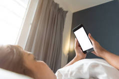 亚洲妇女手用智能手机在卧室里的空白屏幕在早晨.