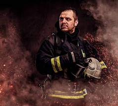 一个穿着制服的职业消防员, 在黑暗的背景下, 在火灾中的火花和烟雾中戴着安全帽.