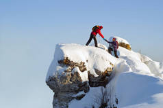 两个徒步旅行者在山顶上过冬;一个男人帮助一个女人爬上一只纯粹的石头