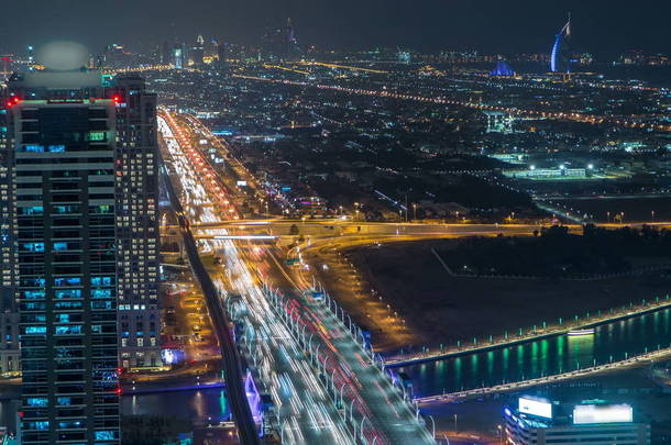 迪拜商业海湾塔照亮的夜晚游戏中<strong>时光倒流</strong>。迪拜水运河桥与谢赫扎耶德道路交通。天台视图的一些摩天大楼和在建的新塔。多云的天空
