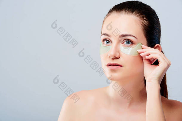 在眼部治疗。妇女面孔与透明质酸水凝胶补丁在眼睛之下。美丽的年轻<strong>女性</strong>与新鲜柔软的皮肤应用<strong>美容</strong>补丁的灰色背景。高分辨率