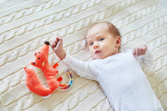 新生女婴躺在针织毯上, 微笑着看着五颜六色的木制拨浪鼓玩具。1月大的孩子在家