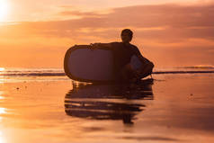 冲浪者坐在海边的冲浪板剪影日落