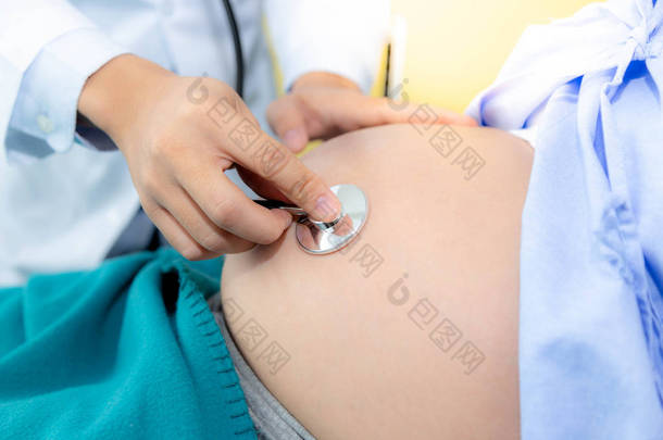 美丽的孕妇躺在医院房间的床上。英俊的医生正在<strong>检查胎儿</strong>的心跳和<strong>胎儿</strong>的位置在母亲的腹部使用听诊器。她下个月就要分娩了。