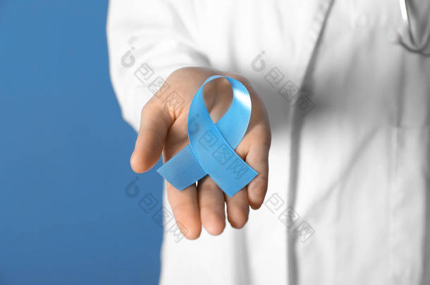 女性医生持有蓝色丝带在颜色背景, 特写镜头。癌症意识概念