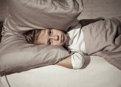 不快乐的女孩覆盖她的耳朵与枕头试图睡在晚上感到不眠之夜悲伤和疲惫的父母争论家庭与儿童睡眠障碍失眠和精神病障碍.