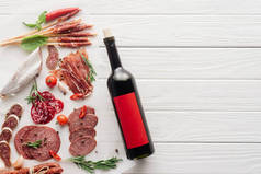 在白色木制桌面上的红酒瓶和各种肉类小吃的顶部视图