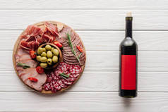 在白色木制桌面上的红酒瓶和各种肉类小吃的顶部视图