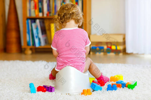 可爱的12个月大的<strong>幼儿</strong>女婴坐在便盆上的衣服。小孩玩教育用的木制玩具.厕所培训的概念。<strong>幼儿</strong>学习、发展步骤