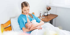 在病房里微笑的年轻母亲母乳喂养新生儿的高视角