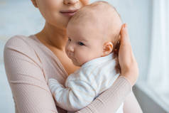 裁剪拍摄快乐的母亲抱着可爱的婴儿在家里
