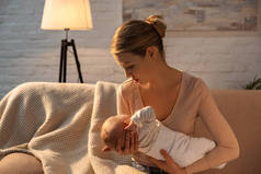 美丽的年轻母亲抱着婴儿在母乳喂养在夜间