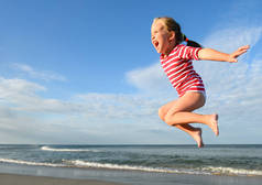 夏天海滩上漂亮的小女孩。快乐的小女孩在蓝天和夏日的背景下在空中跳跃和盘旋。愉快的孩子女孩在海滩玩和有乐趣