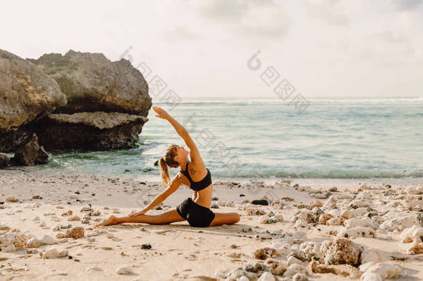 年轻女子在<strong>日</strong>落或<strong>日</strong>出时在海滩练习<strong>瑜伽</strong>.