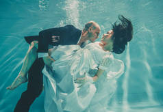 美丽的浪漫夫妇的新娘和新郎结婚后游泳轻轻地在水下和放松