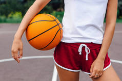 年轻女子穿着白色T恤，短裤在篮球场上拿着球.