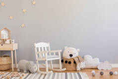 时尚和现代的斯堪的纳维亚新生儿内饰，配有玩具、儿童椅、毛绒犀牛、带泰迪熊的天然篮子和小木架。灰色背景墙，带星形图案.