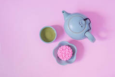 粉红月饼，蓝色茶壶，粉红色背景上的绿茶。中国中秋节食品.