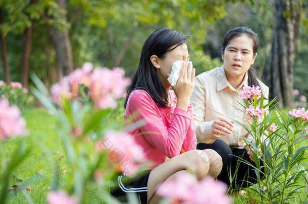 亚洲女童因花粉过敏而在纸巾上打喷嚏，妇女对开花的花朵过敏，少女对室外公园开花树面前的花粉喷鼻涕过敏