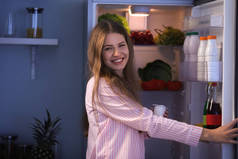 晚上在冰箱里选择食物的美丽的年轻女子