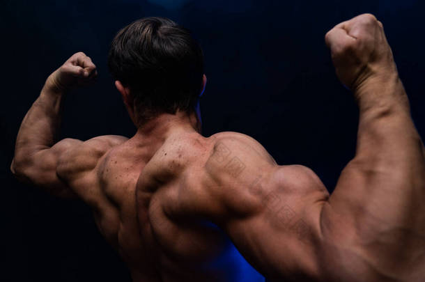 肌肉男子显示肌肉孤立在黑色的背景与有色的烟雾。健康生活方式的概念