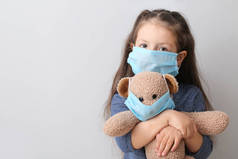 小女孩和泰迪熊，戴着灰色背景的防护口罩