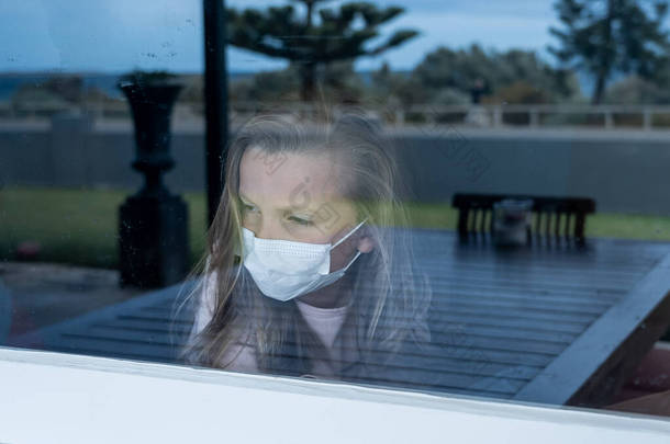 COVID-19封锁。在隔离期间，一个戴着面具的忧郁寂寞小女孩从窗户往外看。可悲的病童在家里孤立无援.Coronavirusu疫情与<strong>儿童心理健康</strong>.