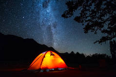 帐篷和夜空。高耸的橙色远足帐篷，繁星繁茂的天空，前景一片光明.