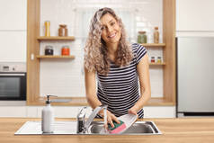 一个年轻女人在厨房用海绵洗盘子的画像