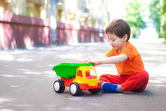 一个男孩在沥青上玩汽车。街上的游戏。孩子们的闲暇时间夏天在城里。一个男孩子夏天在城里散步。那男孩坐在沥青路面上