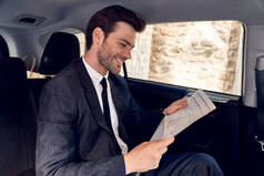 阅读最新消息。一个衣着华丽的年轻人坐在车里看报纸.