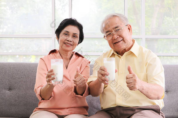 健康的<strong>老</strong>年人生活方式概念。一对健康的亚洲<strong>老夫妻</strong>坐在客厅的沙发上，举着乳白色的眼镜，对着相机，竖起大拇指.