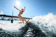 冲浪板上的健美女子在桥的背景下乘风破浪而上