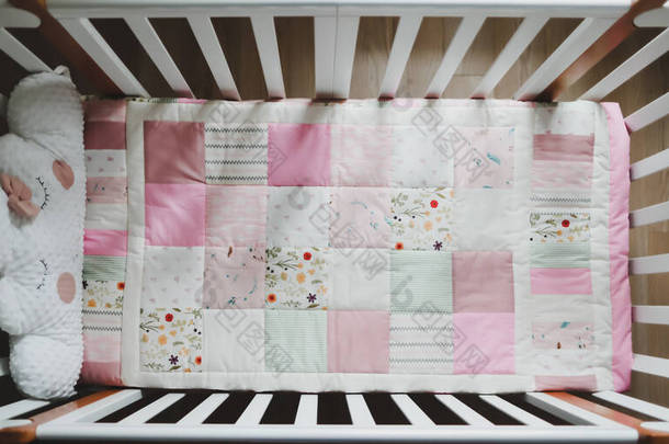 舒适的婴儿床和粉红色的补丁毛毯。儿童保育用床上用品和纺织品。粉红及白色女婴婴儿床照片