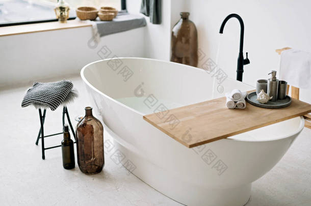在一间风格时尚的阁楼式室内设计，家居装饰的现代公寓里，白色浴缸充满了泡沫水。温泉的概念，放松。软性选择性重点.