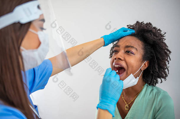 专业医务工作者穿着个人防护设备，用试棒检测妇女是否患有危险疾病。女性在接受Covid-19测试时，张开嘴做面颊和咽部擦拭